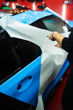 Araba yüzeyini çizik ve ultraviyole ışınlardan korumak için PPF ambalajında koruyucu film katmanı. Detaylandırma merkezinde Araba Paneline ıslak PPF Paketleme