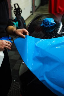 Detaylı uzmanlar mavi PPF filminin kontrollü uygulaması için hidrasyon spreyi kullanırlar. Detaylayıcı mükemmel, kabarcıksız hizalama için canlı mavi vinil sarma uygulamak için sprey destekli yöntem kullanır