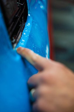 Detaylı merkezdeki araç paneline ıslak plazma yapıştırma. Araba yüzeyini çizik ve ultraviyole ışınlardan korumak için PPF paketleme sırasında koruyucu film katmanı