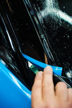 Mavi PPF 'yi bıçakla kesiyorum. Detaylı iş sırasında mavi boya koruma filmini bıçakla kesmek hassas kenarlar sağlar. Detaylı teknisyen mükemmel kontur için bir araba paneli üzerindeki mavi PPF buduyor