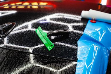 Araba Kaputu 'ndaki PPF Boya Koruma Film Aletleri. Araba ambalajı aletleri, ıslak araba kaputundaki mıknatıslar dahil. Pürüzsüz kapsama için kurulum sırasında PPF ambalajını biçimlendirmek için araç temizleme araçları