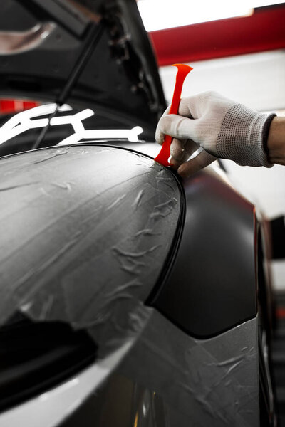 Упаковка автомобиля с помощью инструмента обрезки. Детализация автомобиля применяет виниловую обертку вокруг отделки с помощью пластикового клинового инструмента для бесшовной отделки. Инструмент обрезки для нанесения матовой черной обертки на край панели автомобиля