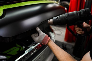 Vinil ambalaj için kullanılan ısı tabancası yapıştırıcıyı aktifleştirir. Isı tabancasıyla arabaya siyah vinil ambalaj uygulamak kesin yapışmayı ve kusursuz yüzey kaplamasını sağlar. Isı Silahıyla Araba Vinili Paketleme