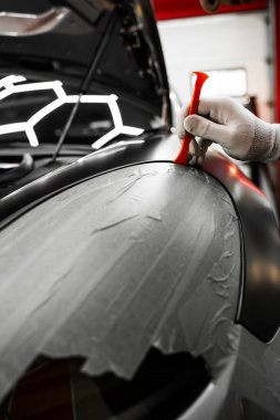 Trim Tool 'la araba sarma. Araç temizleme, pürüzsüz bitiş için plastik takoz aracını kullanarak süsleme etrafına vinil sarma uyguluyor. Bir araba paneli kenarı etrafında mat siyah sargı uygulamak için kırpma aracı