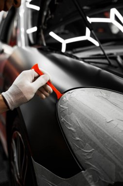 Bir araba paneli kenarına mat siyah sargı uygulamak için kırpma aracı. Trim Tool 'la araba sarma. Araç temizleme, pürüzsüz bitiş için plastik takoz aracı kullanılarak budanma etrafına vinil sarma uygular