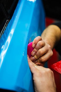 Detaylı uzman, araba yüzeyindeki mavi PPF ambalajını düzleştirmek için kırmızı cam ambalajı kullanır. Araç ambalajı detaylandırması, pürüzsüz, kırışıklıksız yapışma için cırcır böceği darbeleri içerir