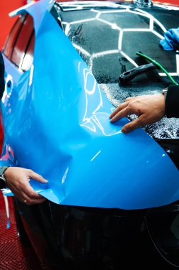 Tüm detaylar sırasında arabaya PPF ambalajı uygulanıyor. Detaylandırma merkezine kalın mavi vinil ambalaj kurulumu. Detaylar hatları sığdırmak için ustalıkla paket uygular ve pürüzsüz, pürüzsüz paket hizalamasını sağlar