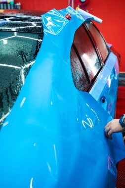 Detaylandırma merkezine kalın mavi vinil ambalaj kurulumu. Detaylar hatları sığdırmak için ustalıkla ambalaj uygular ve pürüzsüz, kusursuz bir paket hizalaması sağlar. Tam ayrıntı sırasında arabaya PPF paketi uygulanıyor