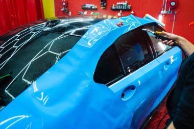 Detaylar hatları sığdırmak için ustalıkla ambalaj uygular ve pürüzsüz, kusursuz bir paket hizalaması sağlar. Tüm detaylar sırasında arabaya PPF ambalajı uygulanıyor. Ayrıntılı merkeze kalın mavi vinil paket kurulumu