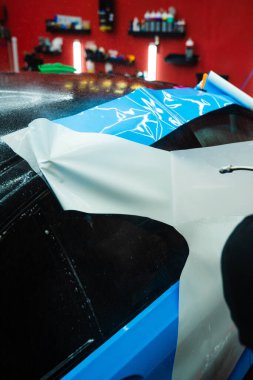 Araba yüzeyini çizik ve ultraviyole ışınlardan korumak için PPF ambalajında koruyucu film katmanı. Detaylandırma merkezinde Araba Paneline ıslak PPF Paketleme