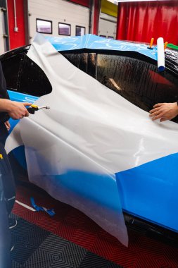 Araba yüzeyini çizik ve ultraviyole ışınlardan korumak için PPF ambalajında koruyucu film katmanı. Detaylandırma merkezinde Araba Paneline ıslak PPF Paketleme
