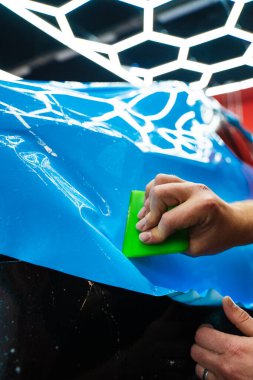 Mavi PPF, yeşil cam sileceği ile arabayı temizlerken ve hasarı engellemek için uygulanmış. Yeşil bir cam sileceği kullanarak yüksek parlak mavi bir PPF uygulamak, arabanın baloncuksuz ve pürüzsüz bir yüzey sağlamasını sağlar