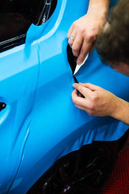 Detaylı teknisyen mavi PPF 'yi mükemmel bir kondisyon için bir araç paneline yerleştirdi. Mavi PPF 'yi bıçakla kesiyorum. Detaylı iş sırasında mavi boya koruma filminin bıçakla kesilmesi hassas kenarları sağlar.