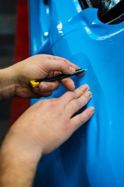 Detaylı teknisyen mavi PPF 'yi mükemmel bir kondisyon için bir araç paneline yerleştirdi. Mavi PPF 'yi bıçakla kesiyorum. Detaylı iş sırasında mavi boya koruma filminin bıçakla kesilmesi hassas kenarları sağlar.