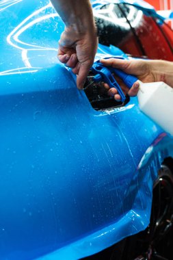 Detaylı uzmanlar mavi PPF filminin kontrollü uygulaması için hidrasyon spreyi kullanırlar. Detaylayıcı mükemmel, kabarcıksız hizalama için canlı mavi vinil sarma uygulamak için sprey destekli yöntem kullanır