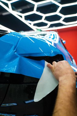 Mavi PPF 'yi bıçakla kesiyorum. Detaylı iş sırasında mavi boya koruma filmini bıçakla kesmek hassas kenarlar sağlar. Detaylı teknisyen mükemmel kontur için bir araba paneli üzerindeki mavi PPF buduyor