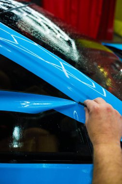 Detaylı iş sırasında mavi boya koruma filmini bıçakla kesmek hassas kenarlar sağlar. Detaylı teknisyen mavi PPF 'yi mükemmel bir kondisyon için bir araç paneline yerleştirdi. Bıçakla mavi PPF kesiliyor