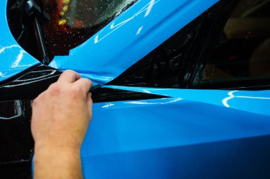 Detaylı teknisyen mavi PPF 'yi mükemmel bir kondisyon için bir araç paneline yerleştirdi. Mavi PPF 'yi bıçakla kesiyorum. Detaylı iş sırasında mavi boya koruma filminin bıçakla kesilmesi hassas kenarları sağlar..
