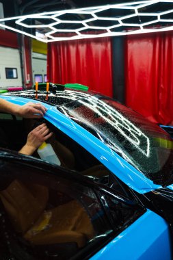 Detaylı uzmanlar mavi PPF filminin kontrollü uygulaması için hidrasyon spreyi kullanırlar. Detaylayıcı mükemmel, kabarcıksız hizalama için canlı mavi vinil sarma uygulamak için sprey destekli yöntem kullanır