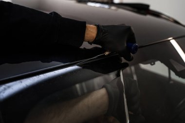 Arabanın ön camını değiştirme işlemi. Ön cam kaldırma işlemi özel kesme kablosu ve kazıma aracı kullanılarak yapılıyor. Otomobil teknisyeni ön camı ince tel ve kazıma bıçağı kullanarak ayırıyor.