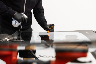 Teknisyen, yeni bir ön camın yüzeyini temizlemek için kazıyıcı kullanıyor. Teknisyen mükemmel yapışmayı sağlamak için yeni ön camı kazıyıp temizliyor.