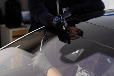 Otomobil teknisyeni ön camı ince tel ve kazıma bıçağı kullanarak ayırıyor. Arabanın ön camını değiştirme işlemi. Özel kesme kablosu ve kazıma aracı kullanılarak ön cam kaldırma işlemi devam ediyor