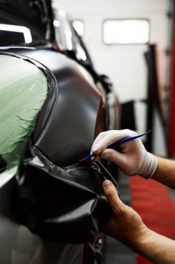 Bir araba paneli kenarına mat siyah sargı uygulamak için kırpma aracı. Trim Tool 'la araba sarma. Araç temizleme, pürüzsüz bitiş için plastik takoz aracı kullanılarak budanma etrafına vinil sarma uygular