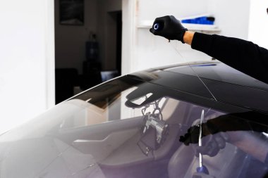 Otomobil teknisyeni ön camı ince tel ve kazıma bıçağı kullanarak ayırıyor. Arabanın ön camını değiştirme işlemi. Özel kesme kablosu ve kazıma aracı kullanılarak ön cam kaldırma işlemi devam ediyor