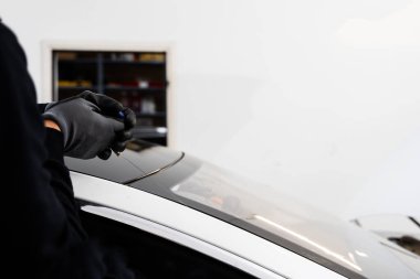 Otomobil teknisyeni ön camı ince tel ve kazıma bıçağı kullanarak ayırıyor. Arabanın ön camını değiştirme işlemi. Özel kesme kablosu ve kazıma aracı kullanılarak ön cam kaldırma işlemi devam ediyor