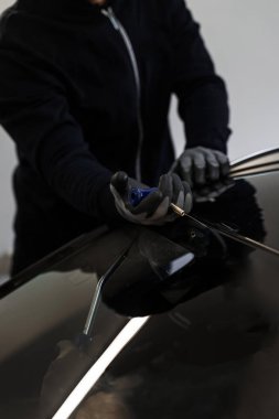 Otomobil teknisyeni ön camı ince tel ve kazıma bıçağı kullanarak ayırıyor. Arabanın ön camını değiştirme işlemi. Özel kesme kablosu ve kazıma aracı kullanılarak ön cam kaldırma işlemi devam ediyor