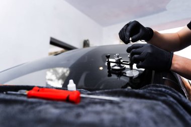 Reçine enjeksiyonuyla ön cam çatlağı onarımı. Teknisyen ön cam enjektörü kullanarak göz çatalını tamir ediyor. Yapısal berraklığı geri getirmek için enjektör uygulaması kullanarak ön camda reçine onarımı