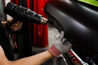 Araba plastiği. Isı tabancasıyla sarılıyor. Isı tabancasıyla arabaya siyah vinil ambalaj uygulamak kesin yapışmayı ve kusursuz yüzey kaplamasını sağlar. Vinil ambalaj için kullanılan ısı silahı yapıştırıcıyı etkinleştirir.