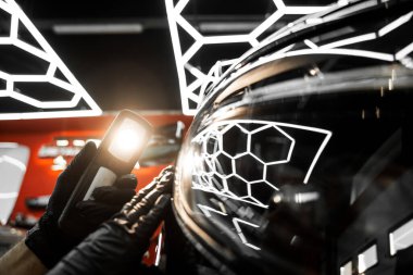 Detaylı bir stüdyoda siyah arabadaki boya sorunlarını tespit etmek için girdap bulucu ışık. Araba boyası denetimi. Araba boyası denetimi cilalama veya seramik kaplamadan önce ayrıntılı denetim ışığı kullanır