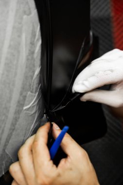 Arabanın plastiği, ön cam bölgesinin yakınındaki keskin kenar budanması ile yerleştirilmiş. Dikkatli kesilmiş bir arabanın üzerine vinil ambalaj kurulumu. Teknisyen pürüzsüz paketleme ve arabanın plastiğini kesme