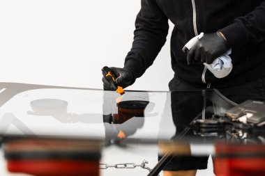 Teknisyen, mükemmel yapışmayı sağlamak için yeni bir ön camı kazıyıp temizliyor. Teknisyen, yeni bir ön camın yüzeyini temizlemek için kazıyıcı kullanıyor.