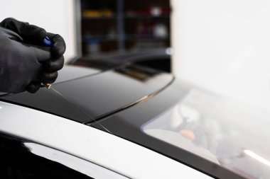 Otomobil teknisyeni ön camı ince tel ve kazıma bıçağı kullanarak ayırıyor. Arabanın ön camını değiştirme işlemi. Özel kesme kablosu ve kazıma aracı kullanılarak ön cam kaldırma işlemi devam ediyor