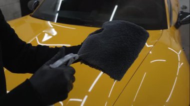 Adam mikro fiber kumaş üzerine araba seramik cilalama için balmumu ürünü spreyler. Detaylı prosedür videosu sırasında. Otomobil servisinde mikrofiberin üzerine mum spreyli araba temizliği..