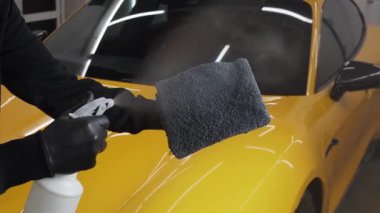Adam mikro fiber kumaş üzerine araba seramik cilalama için balmumu ürünü spreyler. Detaylı prosedür videosu sırasında. Otomobil servisinde mikrofiberin üzerine mum spreyli araba temizliği..