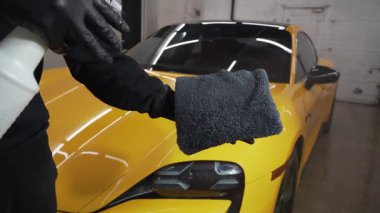 Adam mikro fiber kumaş üzerine araba seramik cilalama için balmumu ürünü spreyler. Detaylı prosedür videosu sırasında. Otomobil servisinde mikrofiberin üzerine mum spreyli araba temizliği..