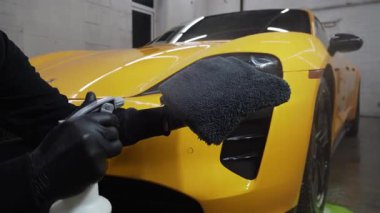 Adam mikro fiber kumaş üzerine araba seramik cilalama için balmumu ürünü spreyler. Detaylı prosedür videosu sırasında. Otomobil servisinde mikrofiberin üzerine mum spreyli araba temizliği..