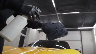 Araba korumasında 4K video için sprey ağda ürünü kullanma süreci. Araba temizleyicisi servisteki mikrofiber kumaşa ağda yapmak için sıvı püskürtüyor..