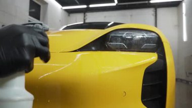 4K video servisinde mikrofiber bezle far parlatma işlemi spor araba detaylandırması. İşçi araba farı cilası için mum sıvısı kullanır.