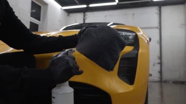 4K video servisinde mikrofiber bezle far parlatma işlemi spor araba detaylandırması. İşçi araba farı cilası için mum sıvısı kullanır.