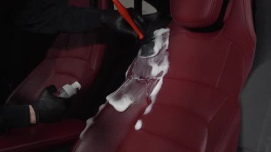İşçi, deri koltuklu 4K video için temizlik solüsyonu ve yumuşak fırça kullanır. Adam, serviste detaylı işlem sırasında deri koltuğu köpük ve fırçayla temizliyor..