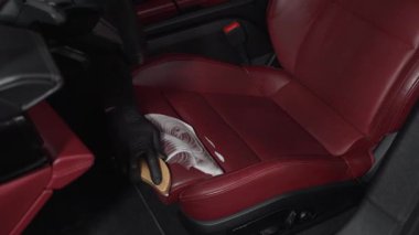 İşçi, deri koltuklu 4K video için temizlik solüsyonu ve yumuşak fırça kullanır. Adam, serviste detaylı işlem sırasında deri koltuğu köpük ve fırçayla temizliyor..