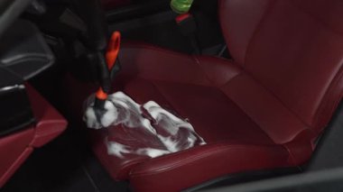 Adam servis videosundaki detaylı işlemler sırasında deri koltuğu köpük ve fırçayla temizliyor. İşçi, deri oto koltuğu için temizlik solüsyonu ve yumuşak fırça kullanır.