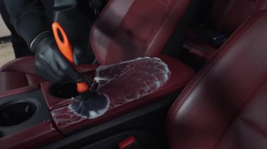 Adam servis videosundaki detaylı işlemler sırasında deri koltuğu köpük ve fırçayla temizliyor. İşçi, deri oto koltuğu için temizlik solüsyonu ve yumuşak fırça kullanır.