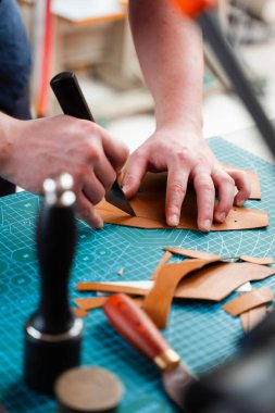 Bıçakla deriyi kesiyor. Zanaatkar deriyi dikkatli bir şekilde hassas aletlerle keser. Zanaatkar deri parçaları ustalıkla hazırlar, deri el yapımı mallar için doğru şablonlar sağlar.