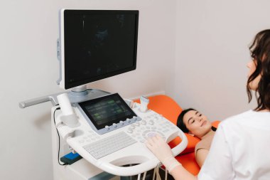 Karın ultrasonu. Jinekolog üreme sağlığı değerlendirmesi için ultrason cihazı kullanıyor. Jinekolog, sakin bir hastaya karın ultrasonu uygular.