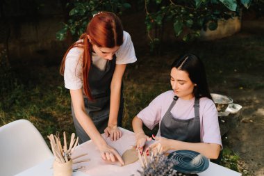 Çömlek Atölyesi Öğretmenliği. Bir seramik atölyesi sırasında çömlek eğitmeni öğrenciye kil şekillendirmede rehberlik ediyor. Seramik eğitim çömlekçilik öğrencilerine rehberlik eden kil sanat uygulamasını vurguluyor